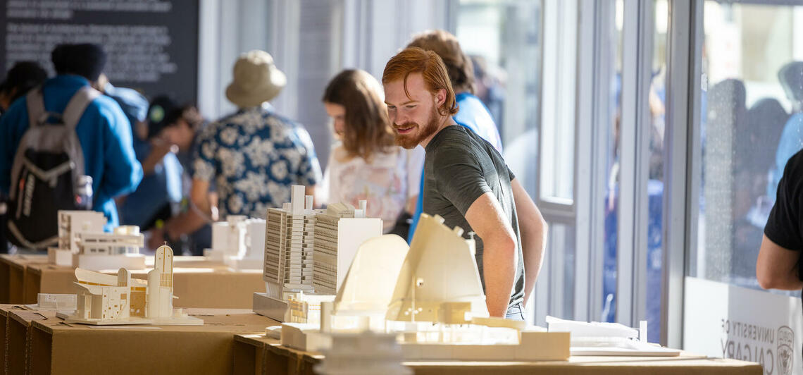 building models on tables in an exhibition room, with people milling about