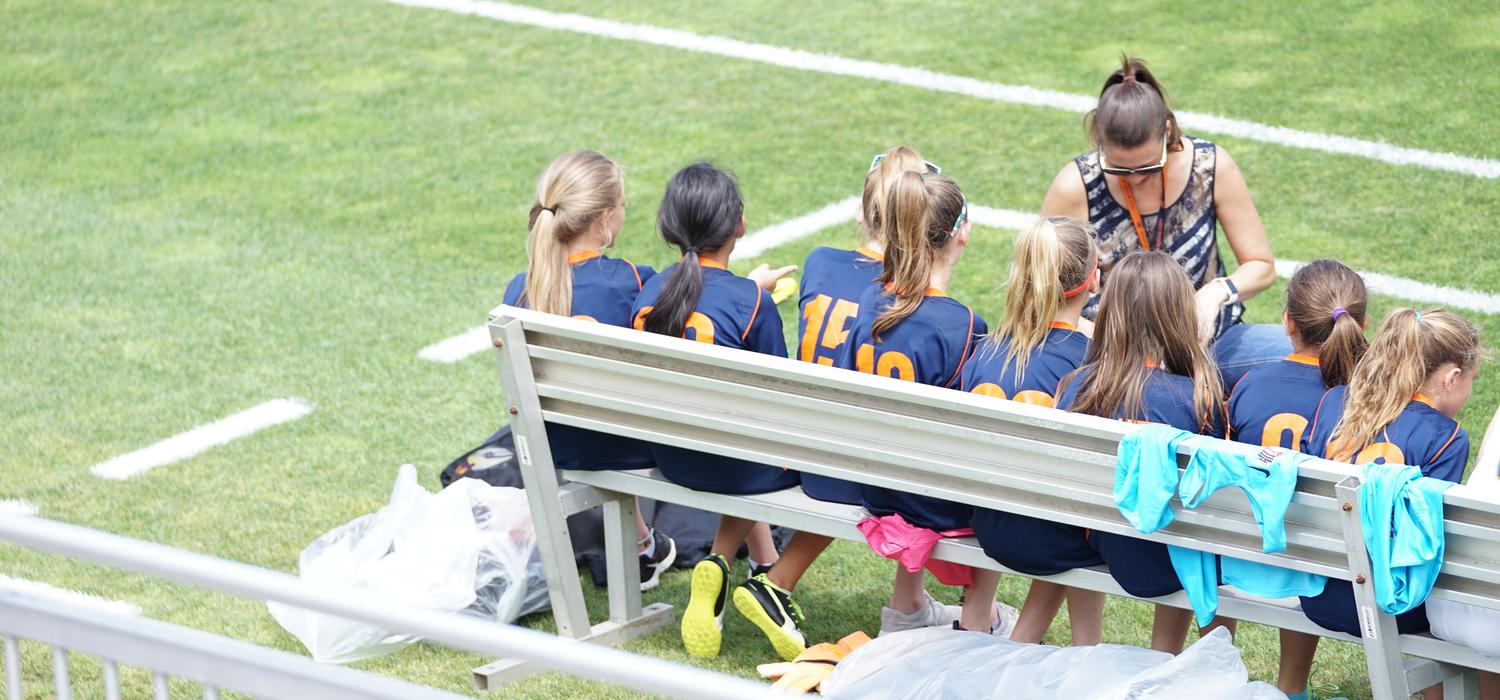 Coach talks to sports team on sidelines of field