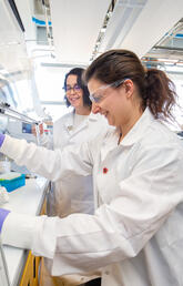 Two people in white lab coats work in a lab