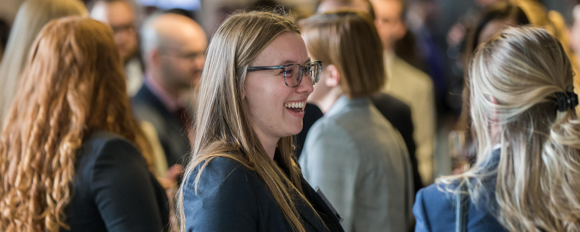 A law student in business attire stands in a crowd, smiling.