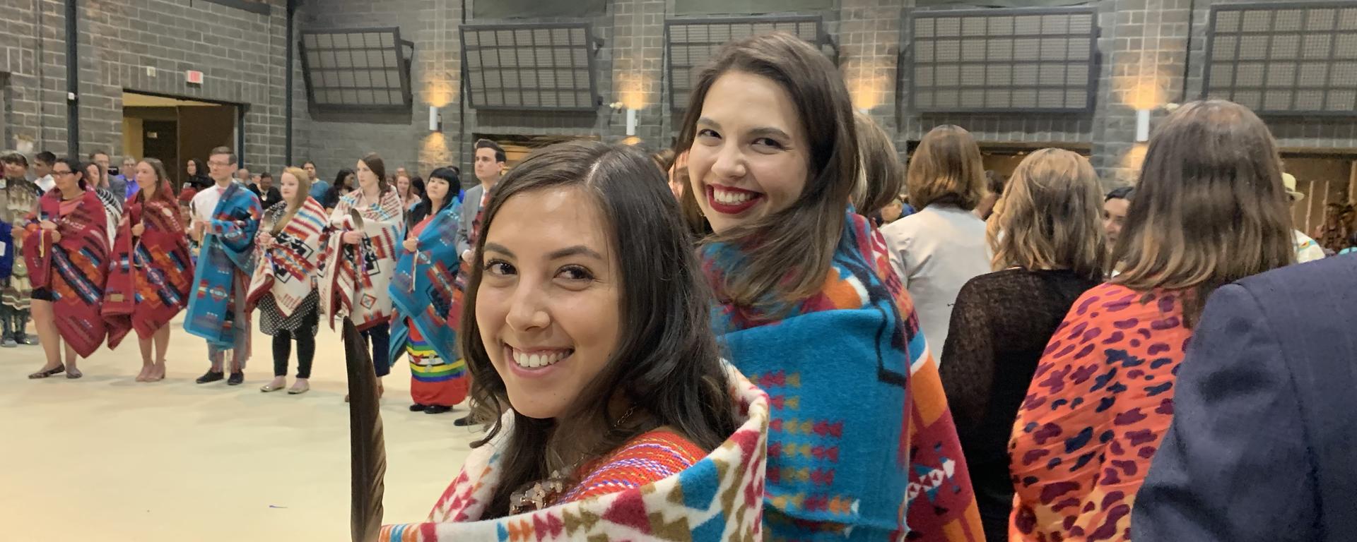 2 law students smile at the camera, in a larger group of students standing in a circle at the Indigenous Convocation ceremony.
