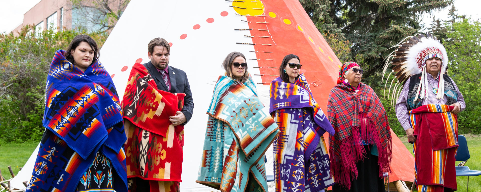 Students and two Elders stand in front of the UCalgary tipi