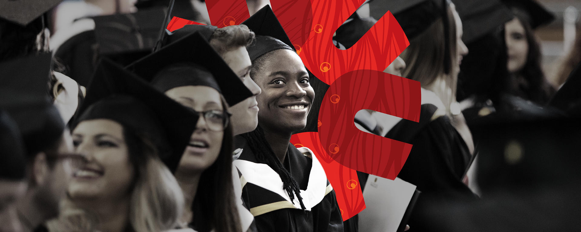 Graduates stand in the gym before the convocation ceremony. They are smiling.