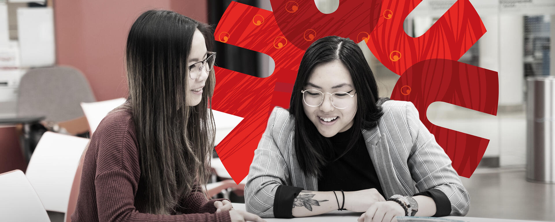 Two students sit at a table looking at a tablet