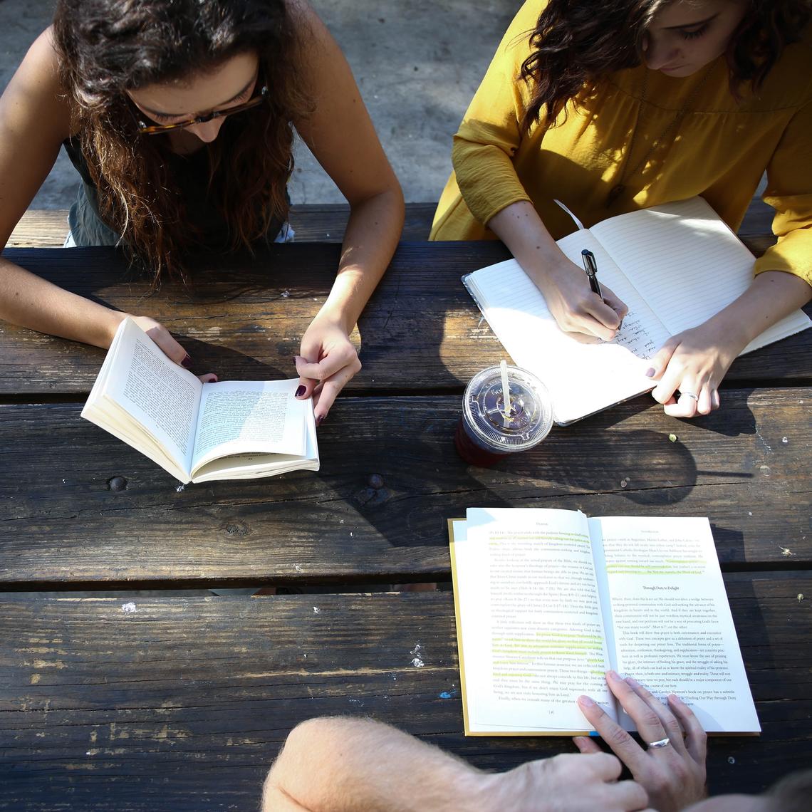 Three people sit at a table reading books