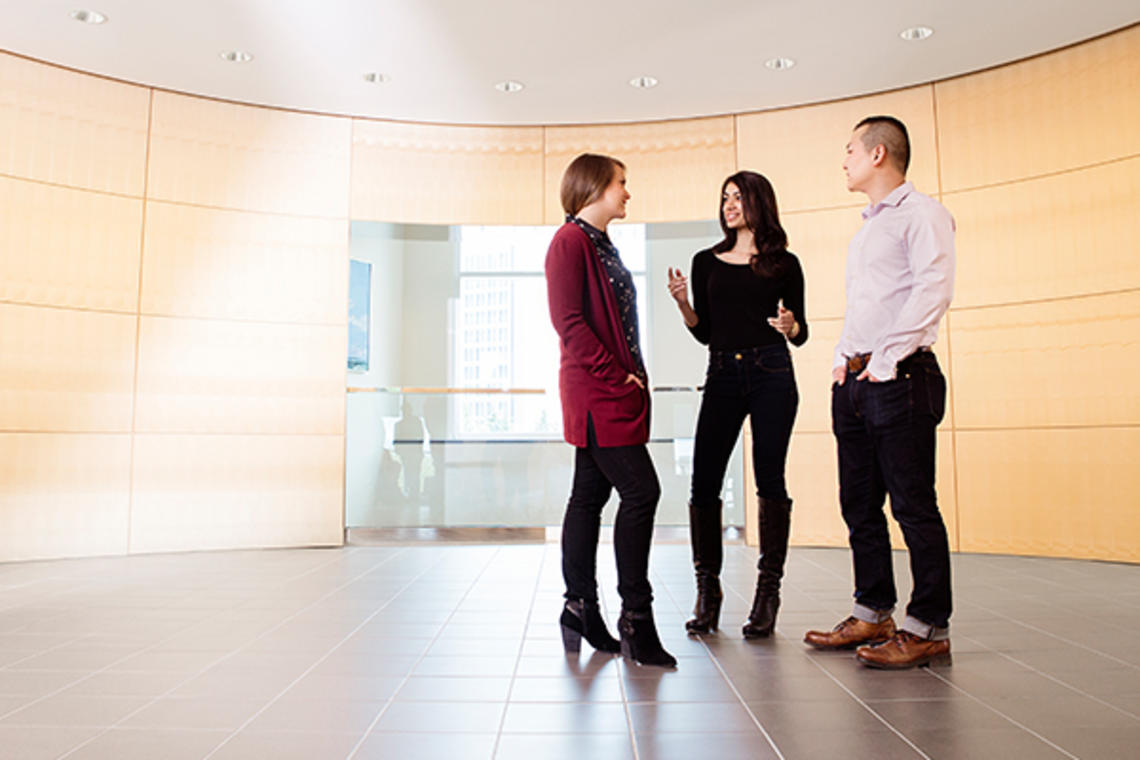 Three students stand in a hallway chatting