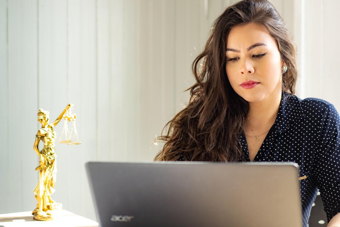 Application requirements A woman sits in front of a laptop. There is a gold statue of lady justice next to her on the table.