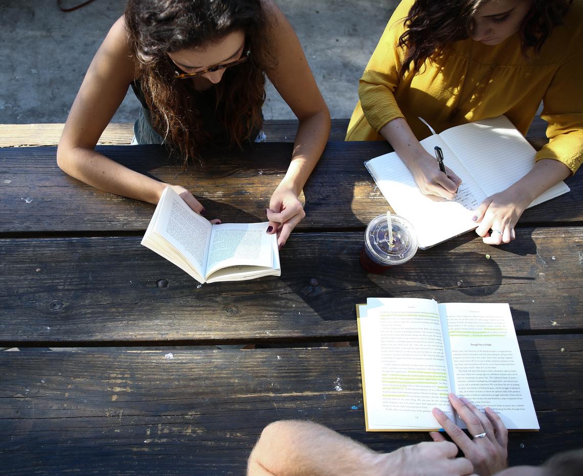 Three people reading books together at a table 