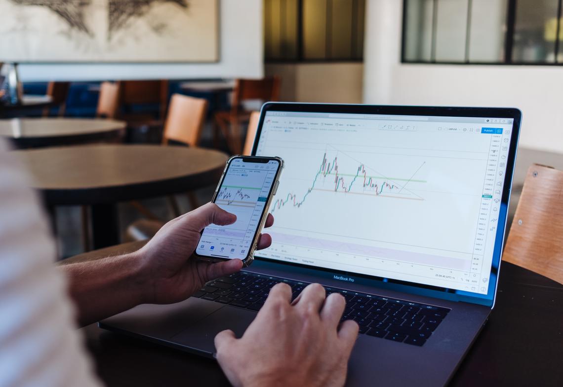 Person holding phone with stock graphs on screen while also on laptop with stock graphs on screen