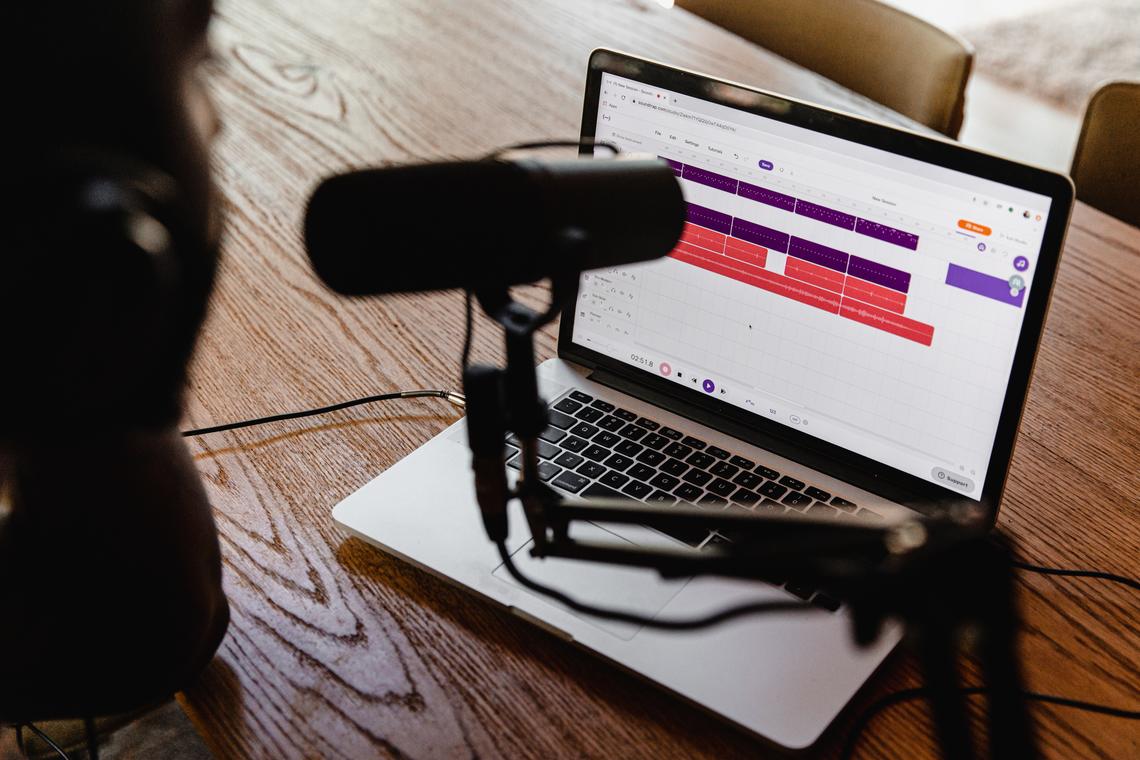 Person recording a podcast with a microphone and laptop