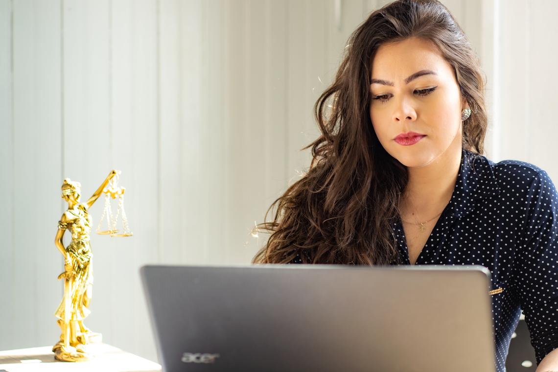 Application requirements A woman sits in front of a laptop. There is a gold statue of lady justice next to her on the table.