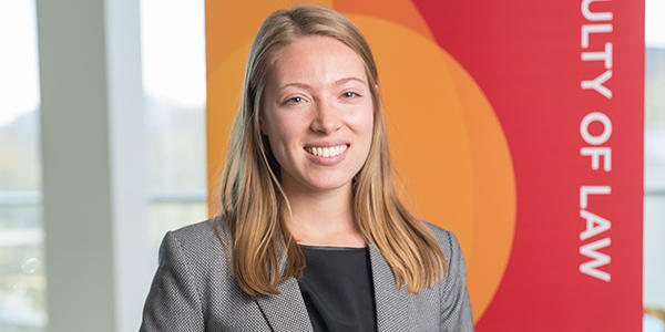 A smiling law student stands in front of an orange and red banner