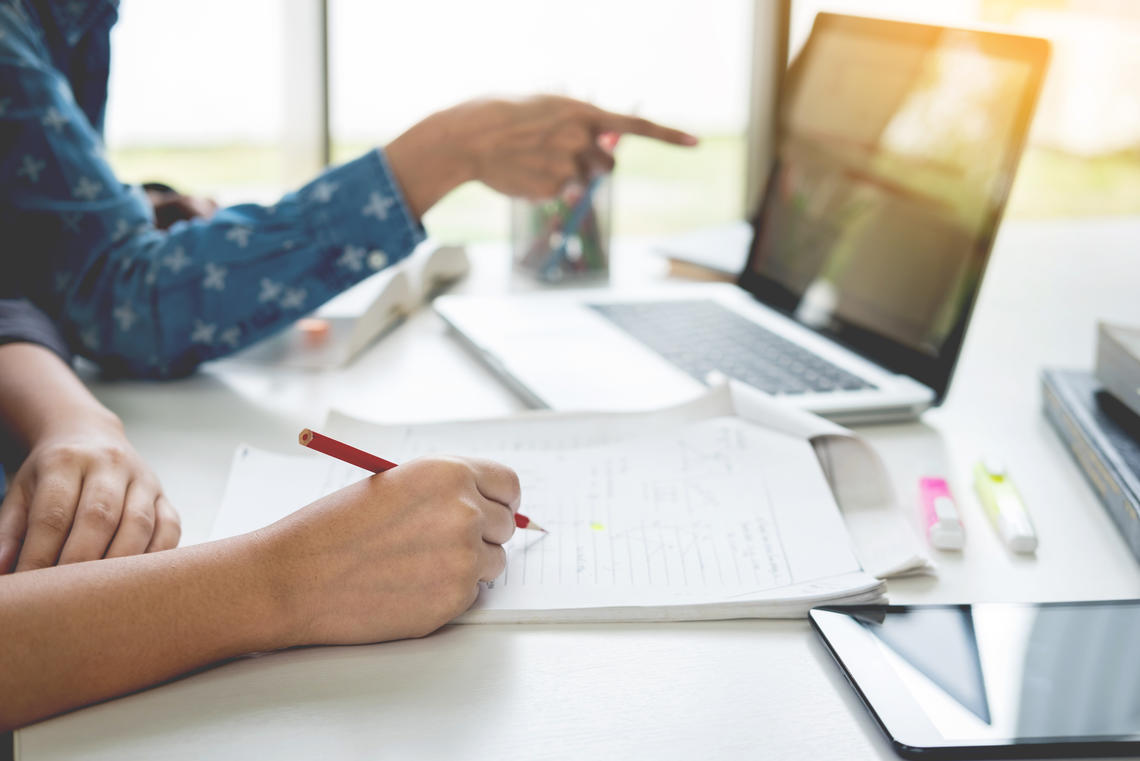 Two people sit at a table with papers and a laptop between them