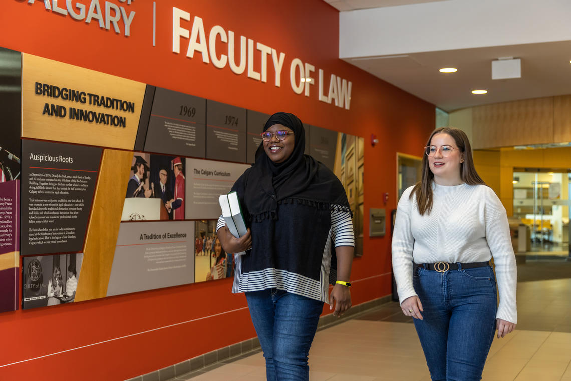 Two students walk past a display on a wall in the law school.