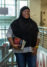 A student holds textbooks while conversing with a classmate