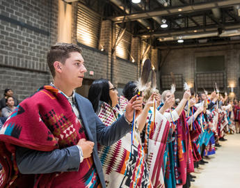 A man stands with an Indigenous blanket in a crowd of people