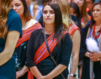 A woman wearing a traditional Metis scarf stands in a crowd