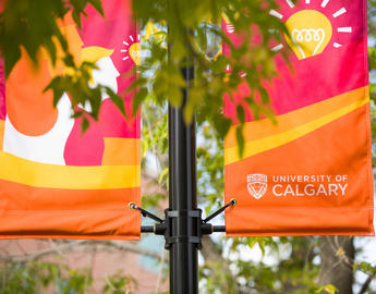 A flag pole on the UCalgary campus has two colourful flags on it.