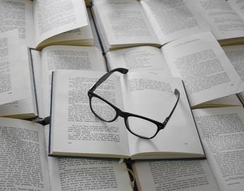 Various open books with a pair of glasses resting on top