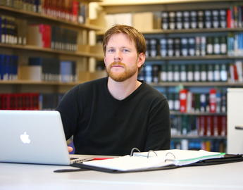Student in library with laptop and binder out on desk
