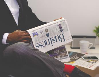 Person sitting with legs crossed and reading a business newspaper