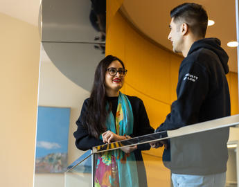 Two students talk to each other in a hallway.
