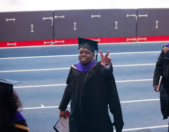 A student in convocation robes gives the peace sign to the camera.