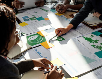 Close up of a busy desktop with papers, sticky notes, and writing utensils.